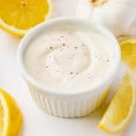 a round ramekin filled with homemade lemon aioli, surrounded by lemon wedges.