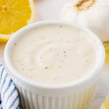 a round ramekin filled with homemade lemon aioli, surrounded by lemon wedges.