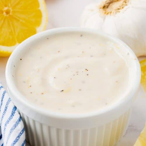 a round ramekin filled with homemade lemon aioli, surrounded by lemon wedges.