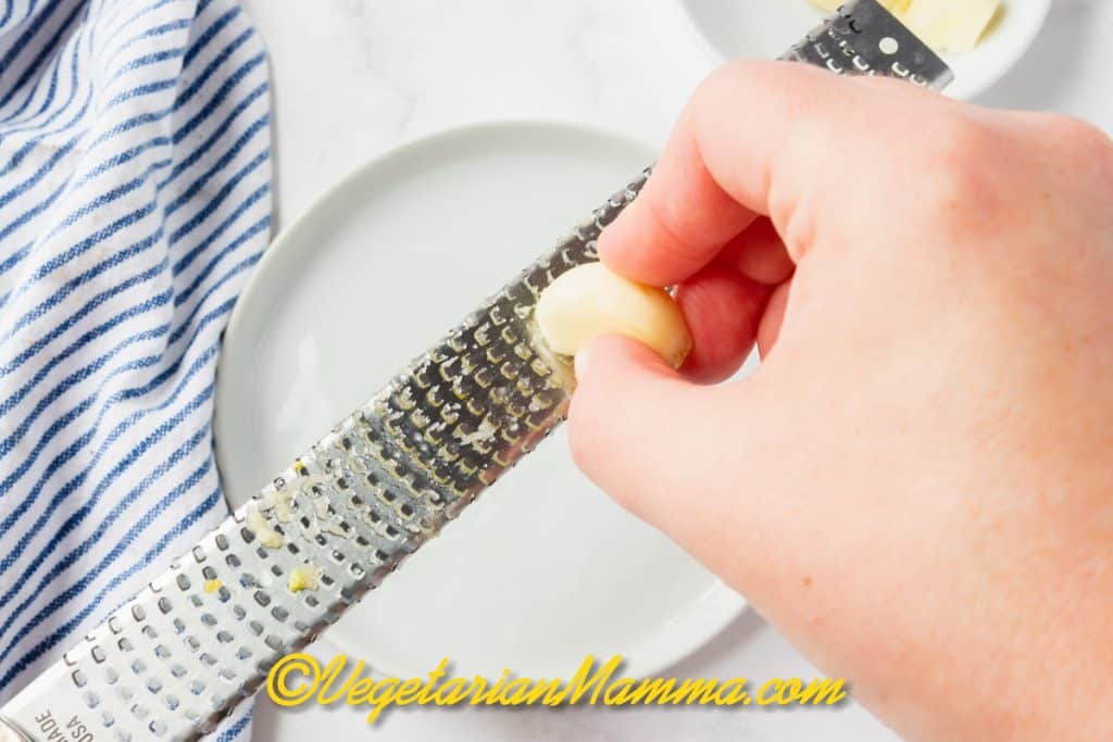 Use a microplane to grate the garlic very finely. You can also use a garlic press or a mortar and pestle to grind the garlic to a paste.
