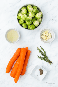 The ingredients needed for Roasted Carrots and Brussel Sprouts, on a marble counter, viewed from above