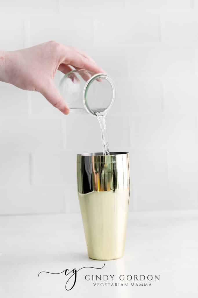 clear liquid being poured into a gold drink shaker