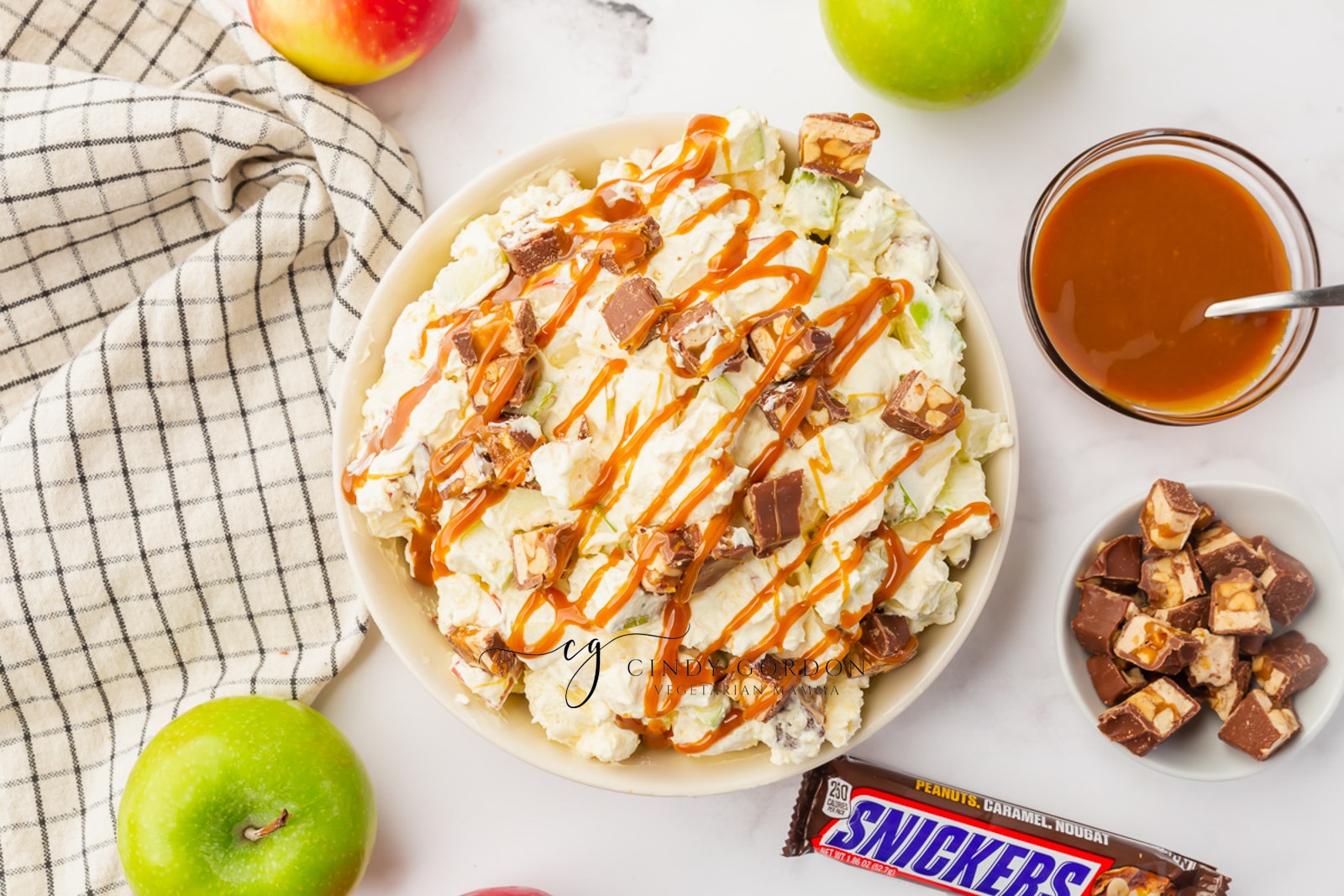 white bowl filled with fully white stuff, apple chunks snicker chunks and caramel syrup. On the side is red and green apples
