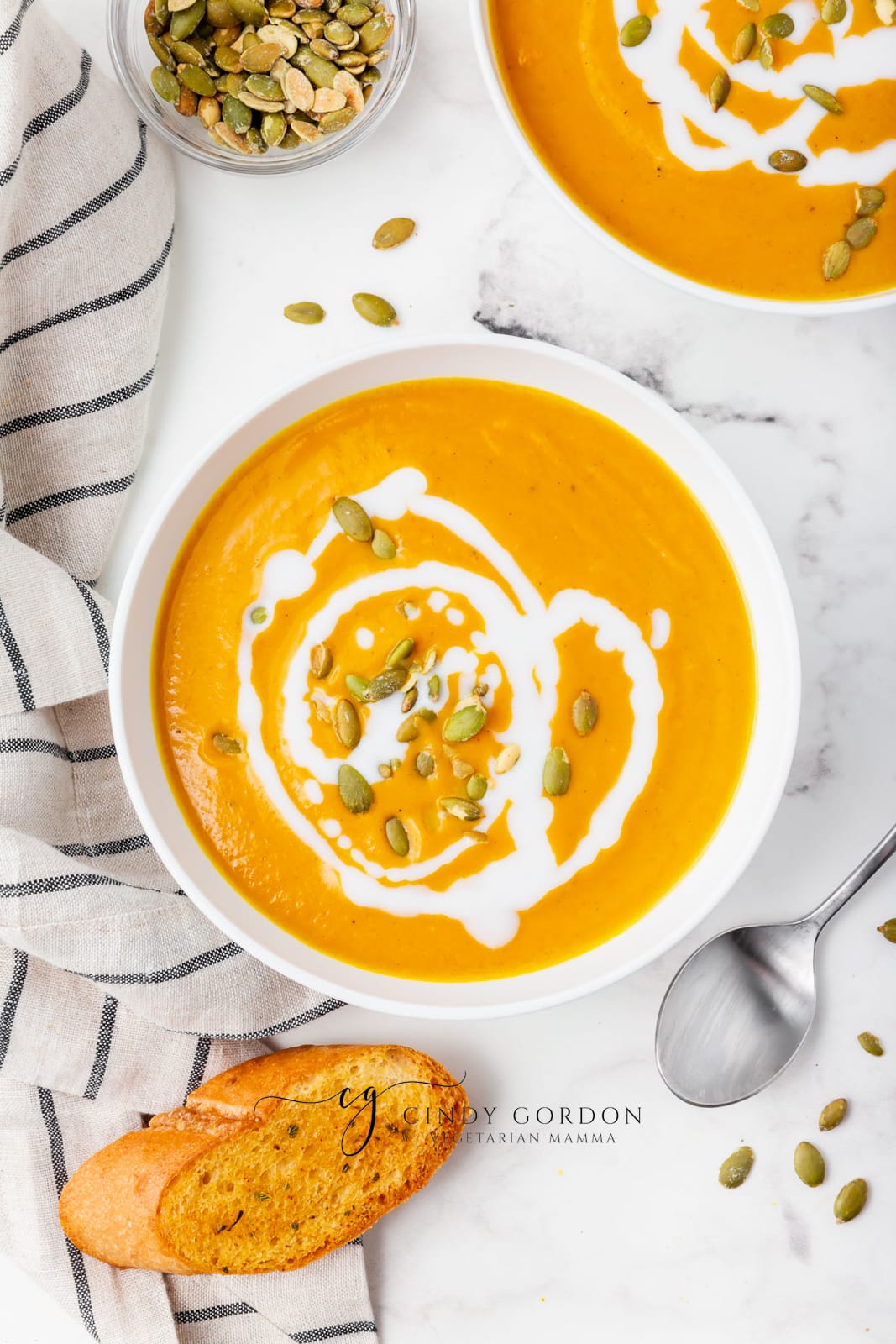 pumpkin bisque in a white bowl with white sauce drizzeled on top