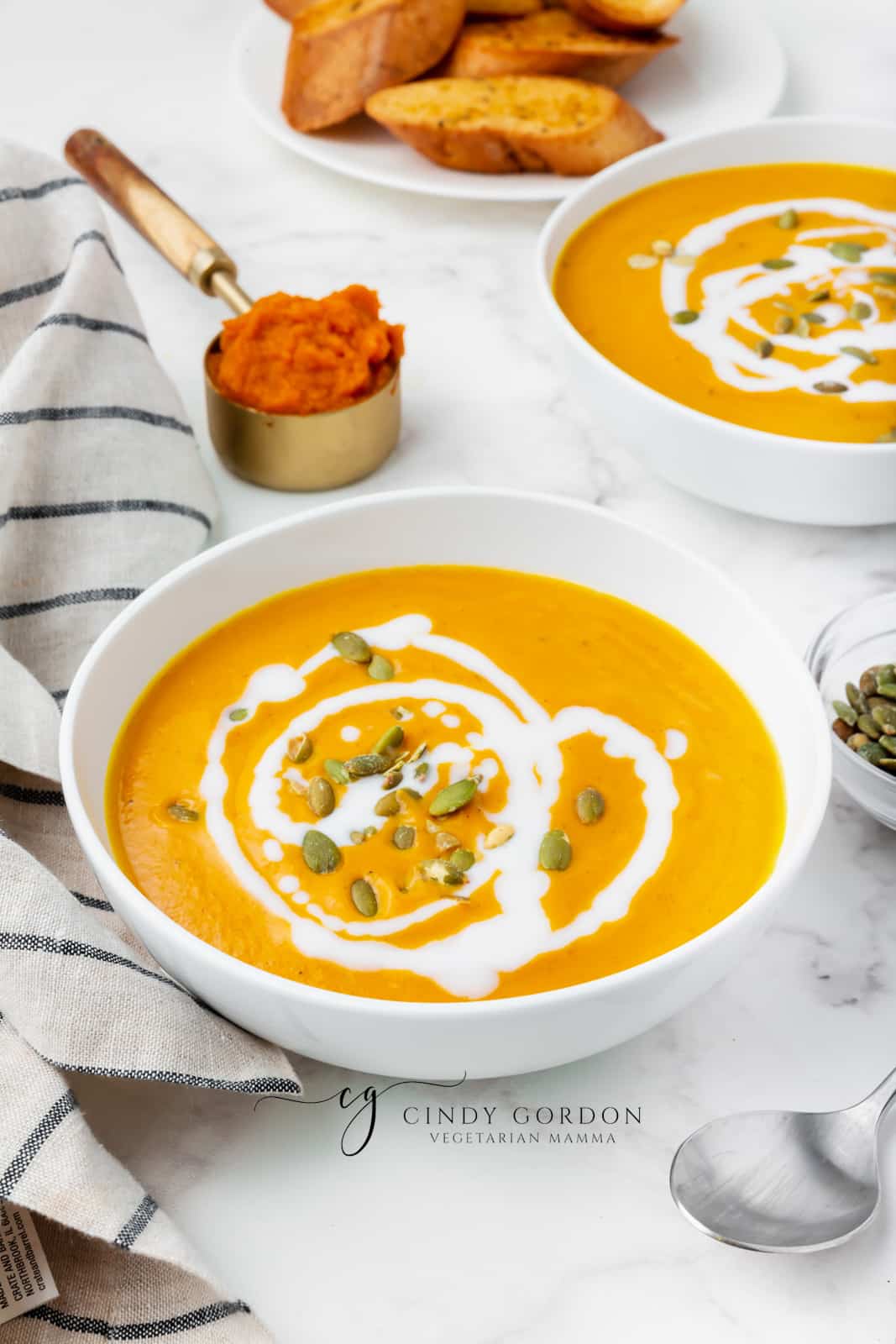 pumpkin bisque in a white bowl with white sauce drizzeled on top