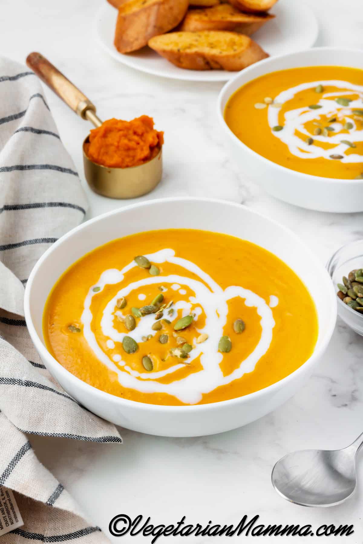 pumpkin bisque in a white bowl with white sauce drizzled on top