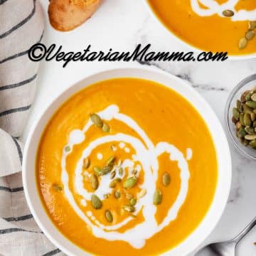 pumpkin bisque in a white bowl with white sauce drizzled on top