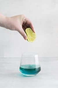 lime being squeezed into a glass with blue liquid