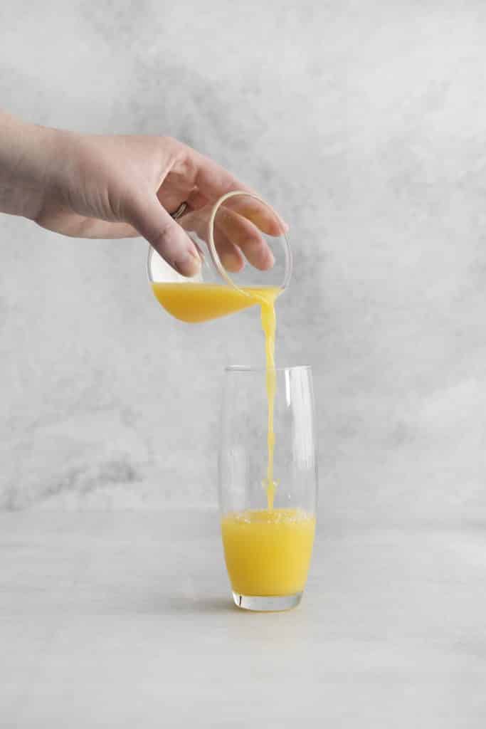 hand pouring orange juice into glass