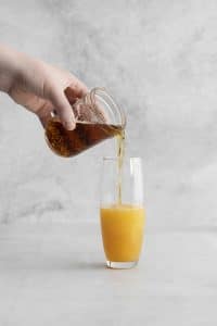 hand pouring dark brown liquid into orange juice