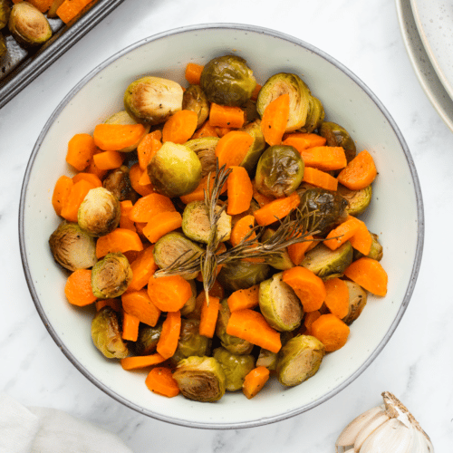 a round bowl filled with perfectly roasted brussel sprouts and sliced carrots