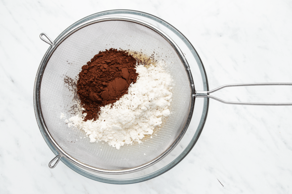 flour and cocoa powder being sifted together in a wire mesh strainer