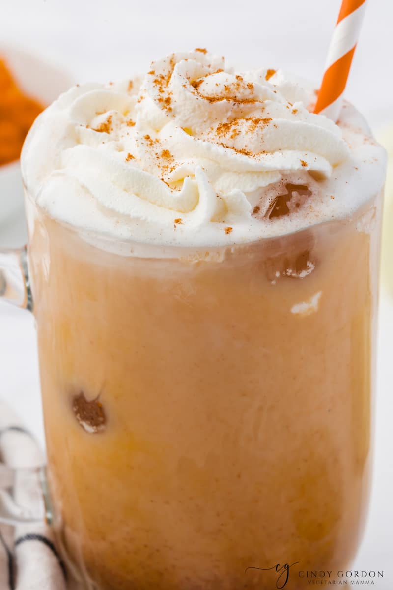 Closeup of a homemade iced pumpkin spice latte with an orange and white striped straw