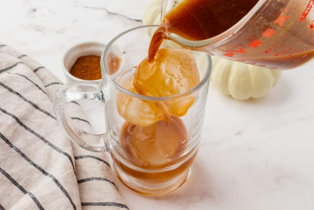 A glass of ice being filled with pumpkin spice coffee