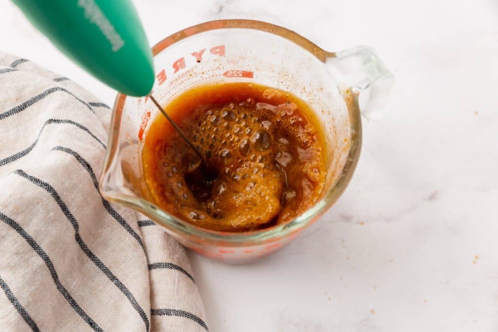 Coffee, pumpkin, and spices being stirred in a measuring cup to make a latte