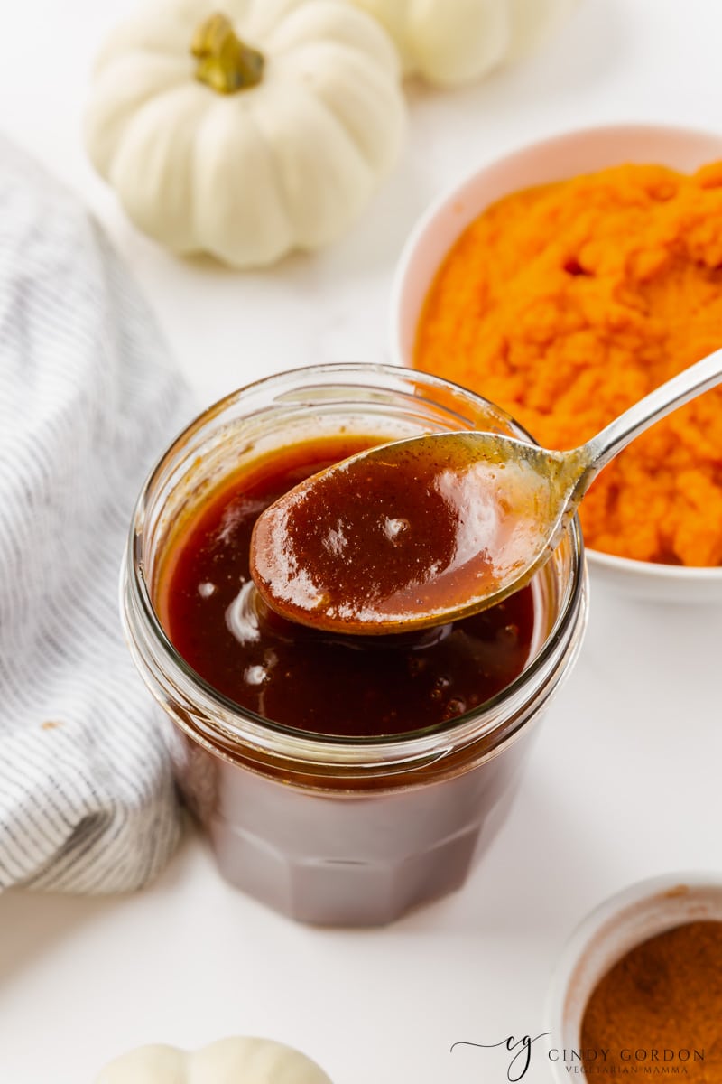 a small jar filled with thick pumpkin syrup next to a bowl of pureed pumpkin.