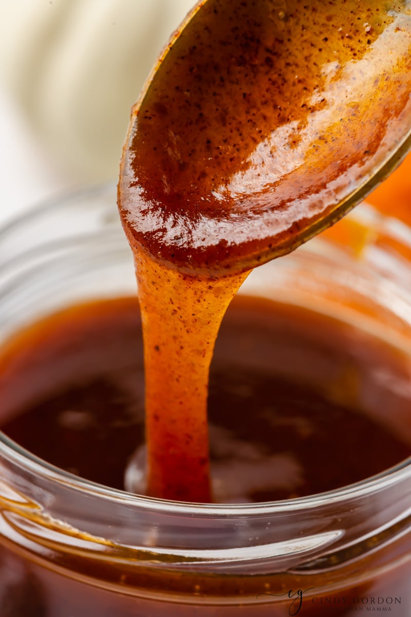 closeup view of spiced pumpkin syrup dripping from a spoon into a glass jar