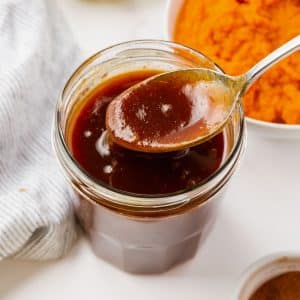 a small jar filled with thick pumpkin syrup next to a bowl of pureed pumpkin.