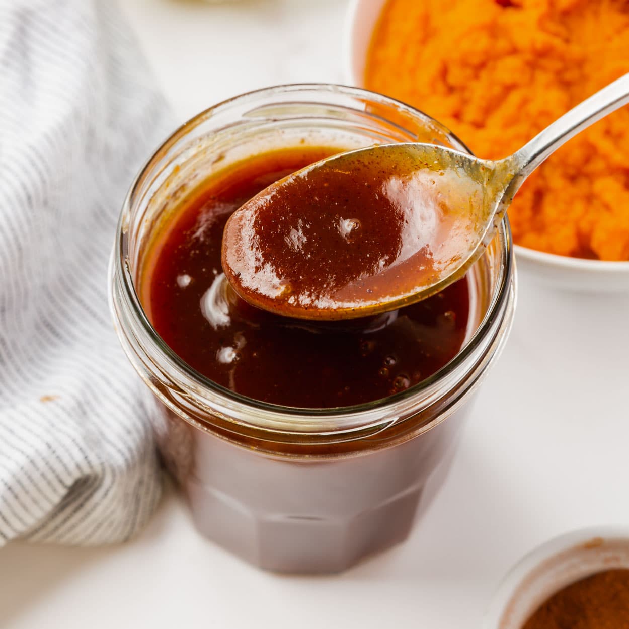 a small jar filled with thick pumpkin syrup next to a bowl of pureed pumpkin.