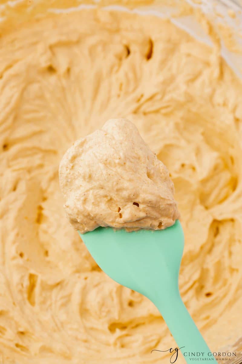 Closeup of a batch of pumpkin whipped cream scooped with a green rubber spatula.