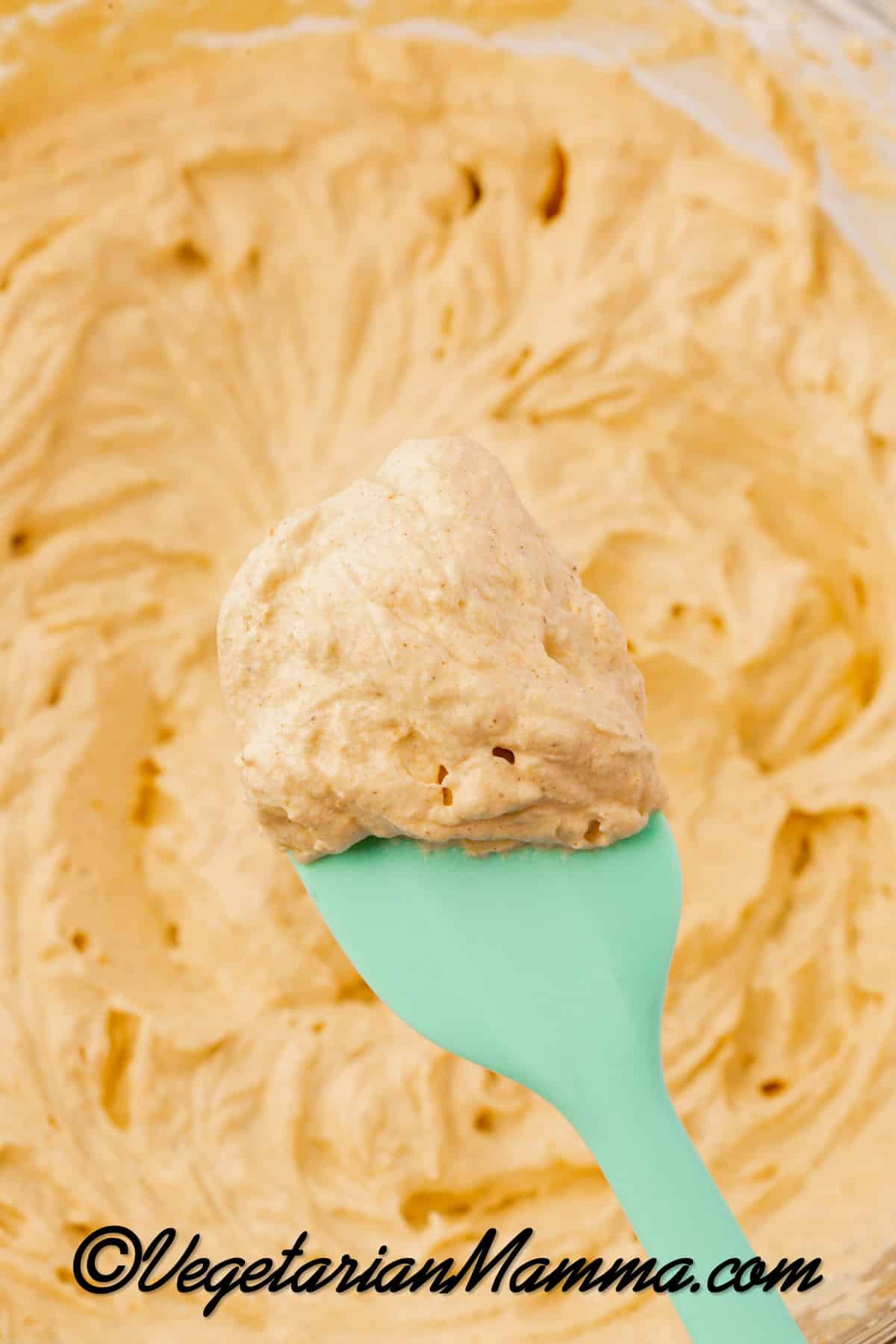 Close-up of a batch of pumpkin whipped cream scooped with a green rubber spatula.