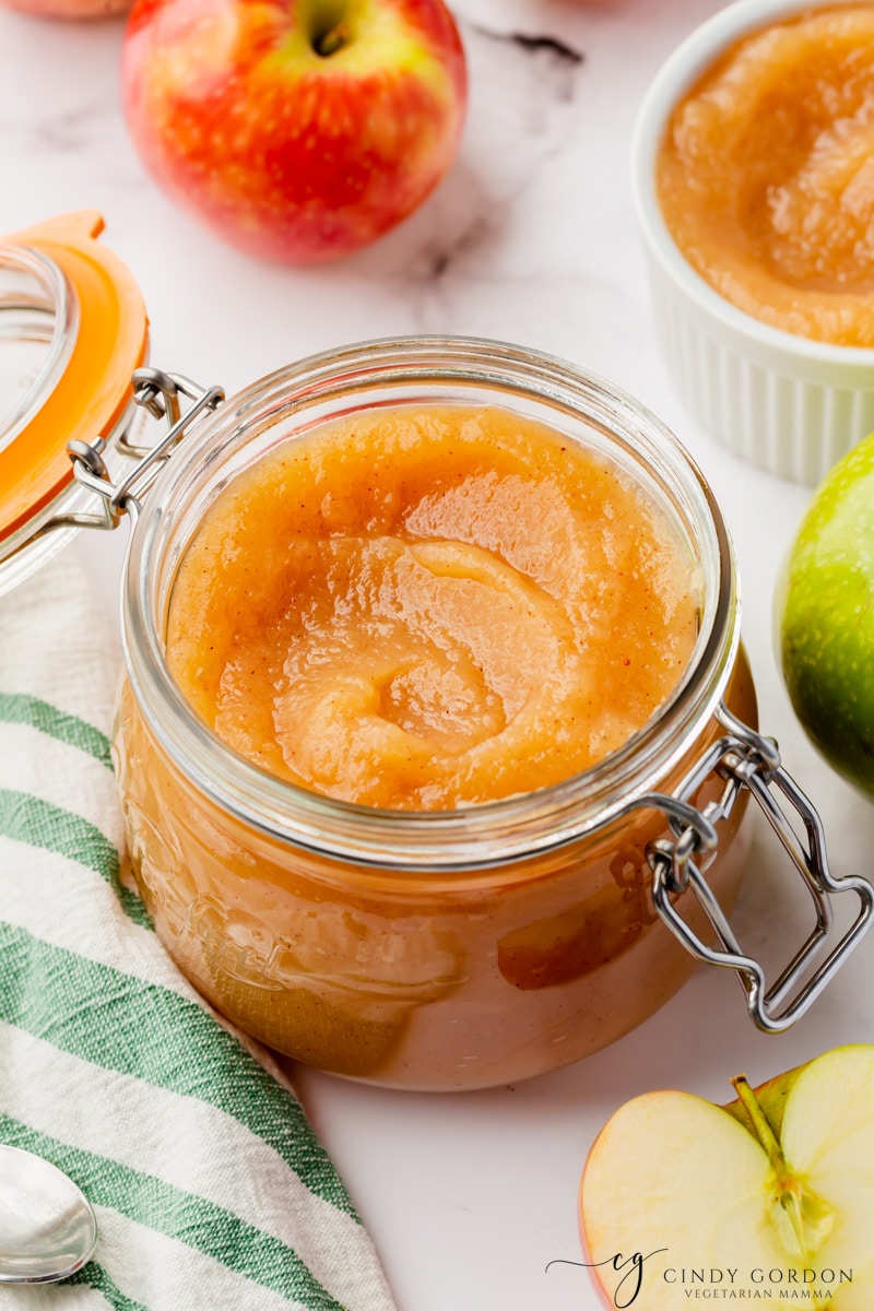 a lidded glass jar filled with homemade unsweetened applesauce. Around the jar are fresh apples. 