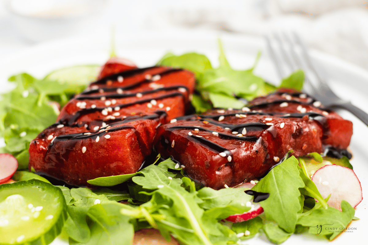 a plate of salad topped with watermelon steak, viewed from the side