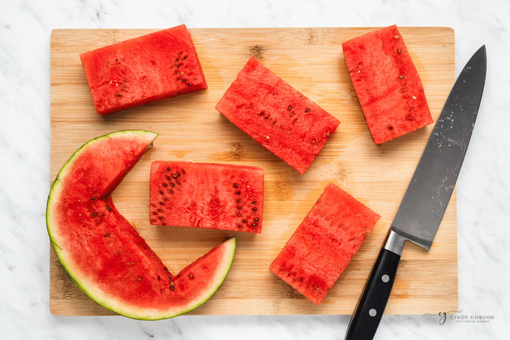 rectangular watermelon steaks being cut on a bamboo cutting board