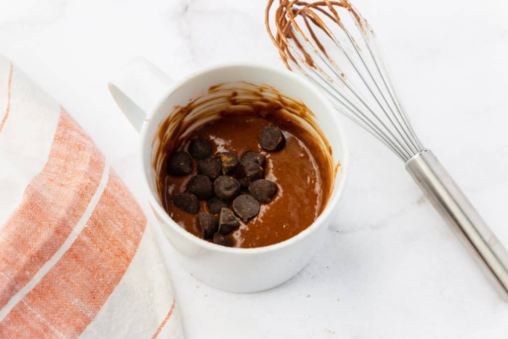 cake batter topped with chocolate chips in a white mug.