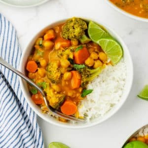 a white bowl of pumpkin curry over rice, with lime wedges on the side. A fork is in the bowl.