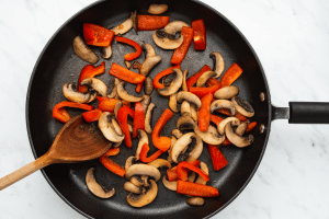 mushrooms and red peppers sauteing in a pan.