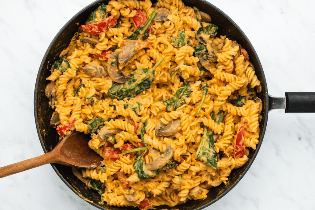 Pasta mixed with sweet potato sauce spinach and other veggies, in a frying pan.