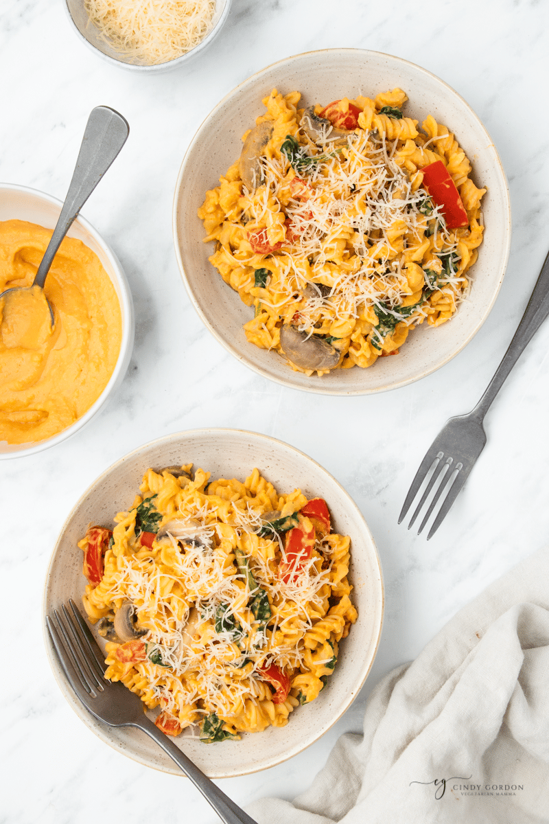 two bowls of pasta with sweet potato sauce on a table, viewed from overhead