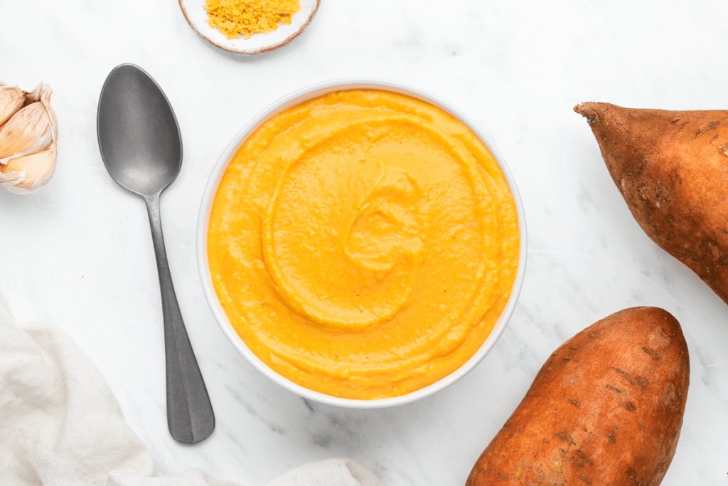 a bowl of creamy sweet potato sauce on a marble countertop, viewed from above