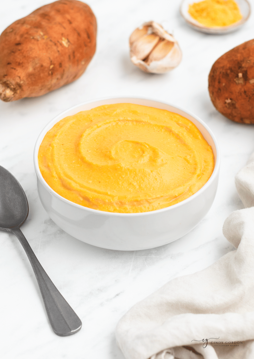 a bowl of sweet potato sauce, surrounded by sweet potatoes and garlic cloves