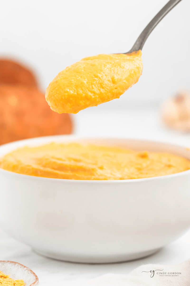 a spoon holding up sweet potato sauce over a bowl of sauce to show how thick and creamy it is