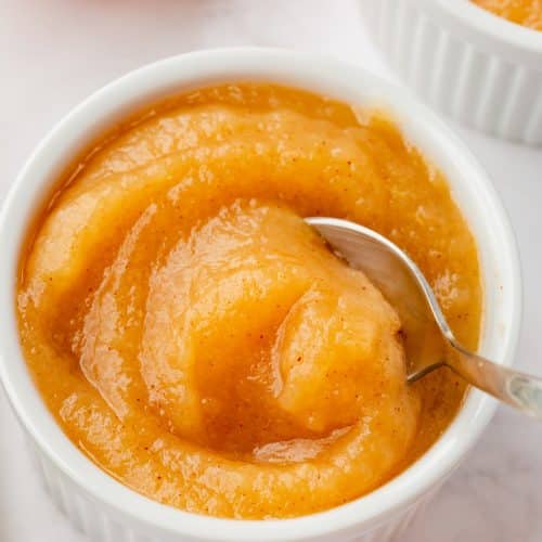 A white cup of delicious apple sauce with a spoon.