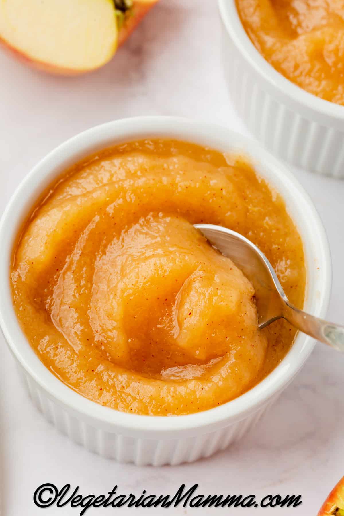 A white cup of delicious apple sauce with a spoon.