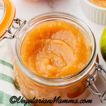 A lidded glass jar filled with homemade unsweetened applesauce. Around the jar are fresh apples.