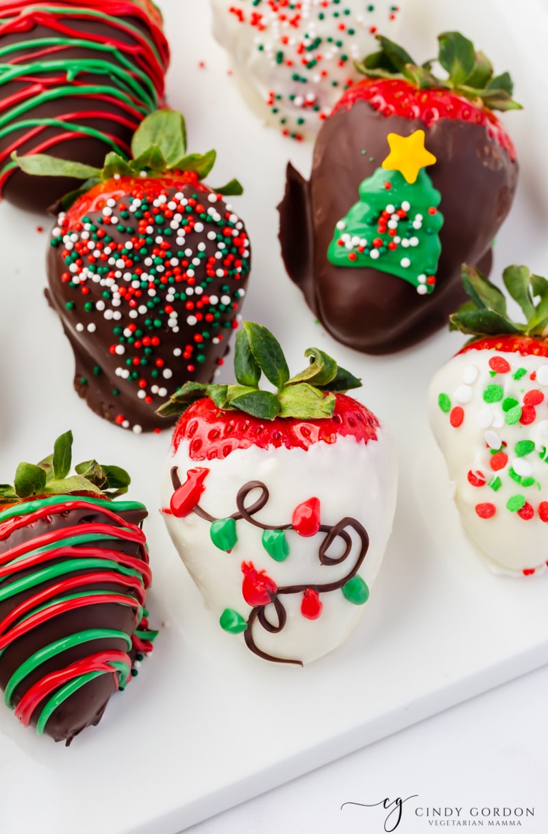 Strawberries covered in white and milk chocolate with christmas decorations,  and sprinkles on them. 