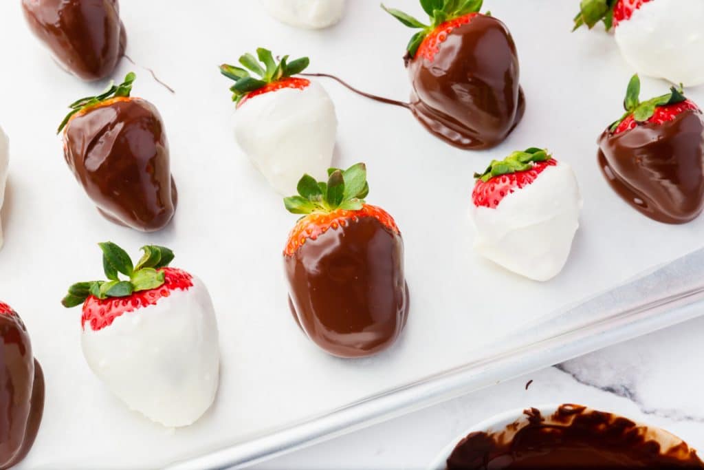 strawberries dipped in white and dark chocolate, on a pan lined with parchment paper