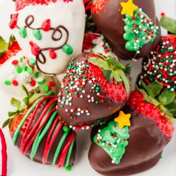 Christmas decorated chocolate covered strawberries stacked on top of each other. Some have sprinkles, two have christmas trees, others have intricate designs.
