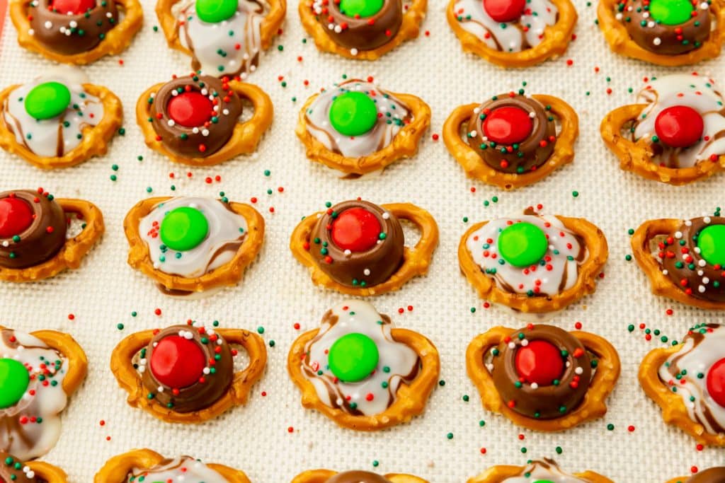 mini pretzels topped with melted kisses and hersheys hugs, topped with red and green m&Ms and sprinkles.