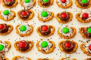mini pretzels topped with melted kisses and hersheys hugs, topped with red and green m&Ms and sprinkles.