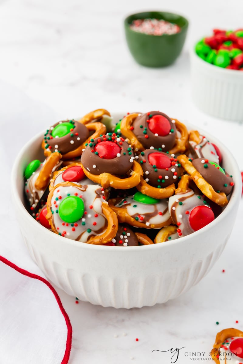 a white bowl filled with christmas pretzels topped with chocolate kisses and m&ms.