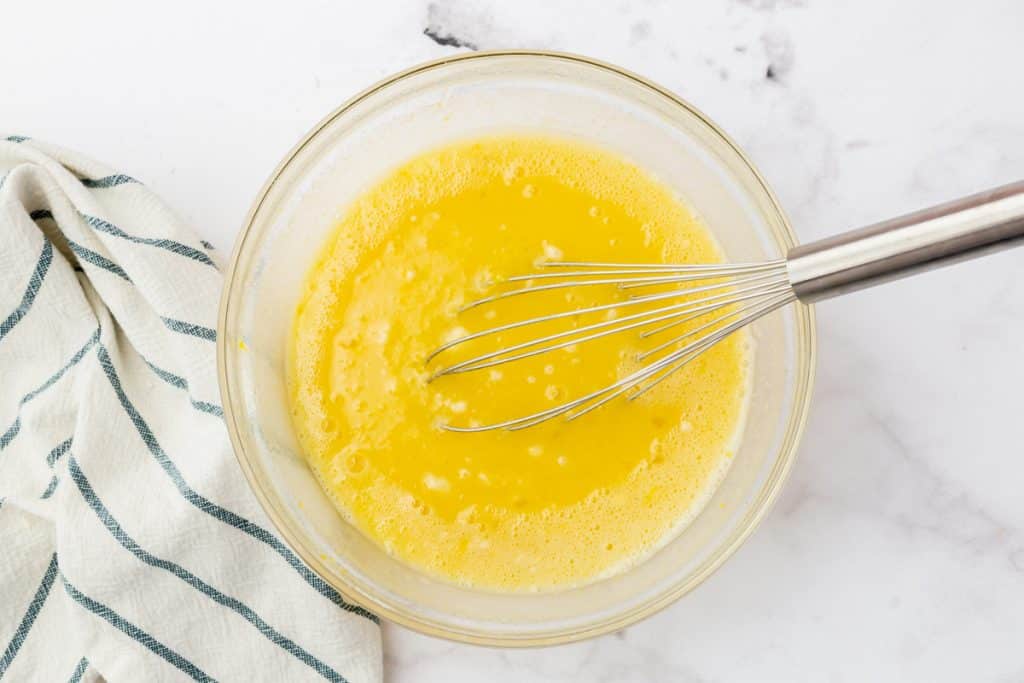 a glass bowl with lemon bar filling being whisked.