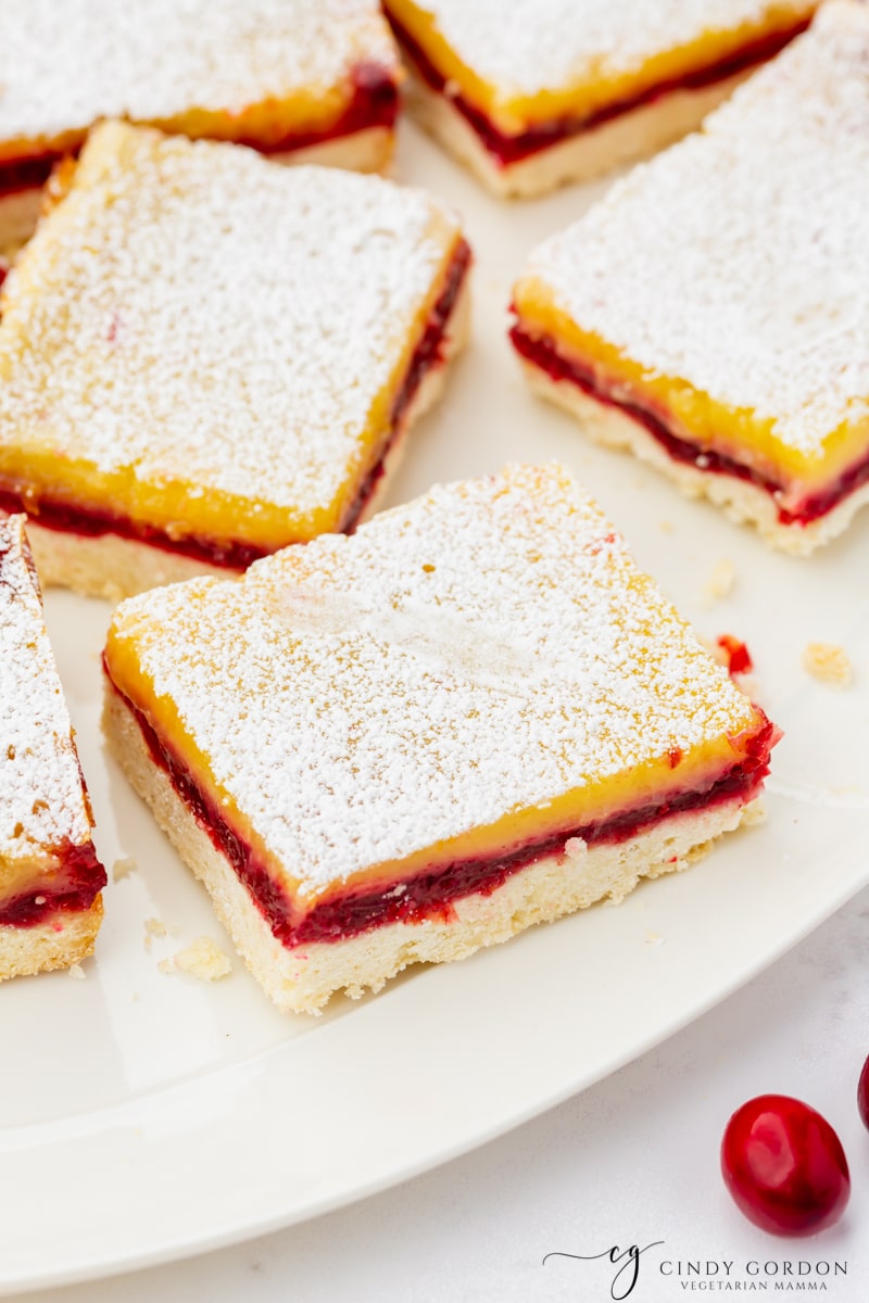 cranberry lemon bars sprinkled with powdered sugar in a single layer on a platter.