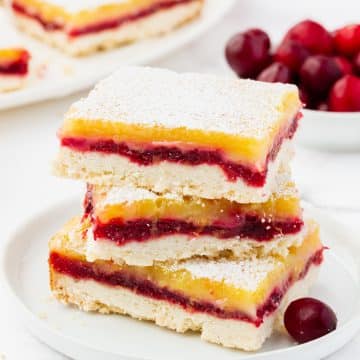 a large rectangle lemon bar with cranberry filling, dusted with powdered sugar, next to other squares of cranberry lemon bars.