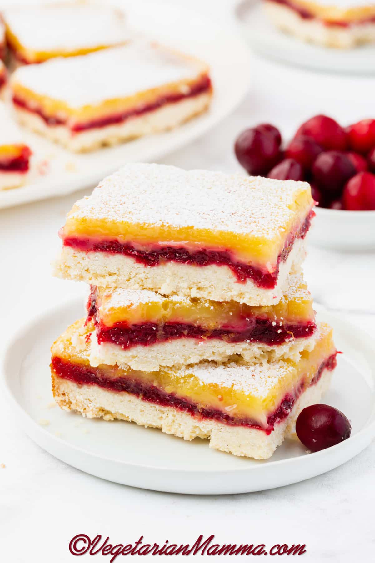 a large rectangle lemon bar with cranberry filling, dusted with powdered sugar, next to other squares of cranberry lemon bars.