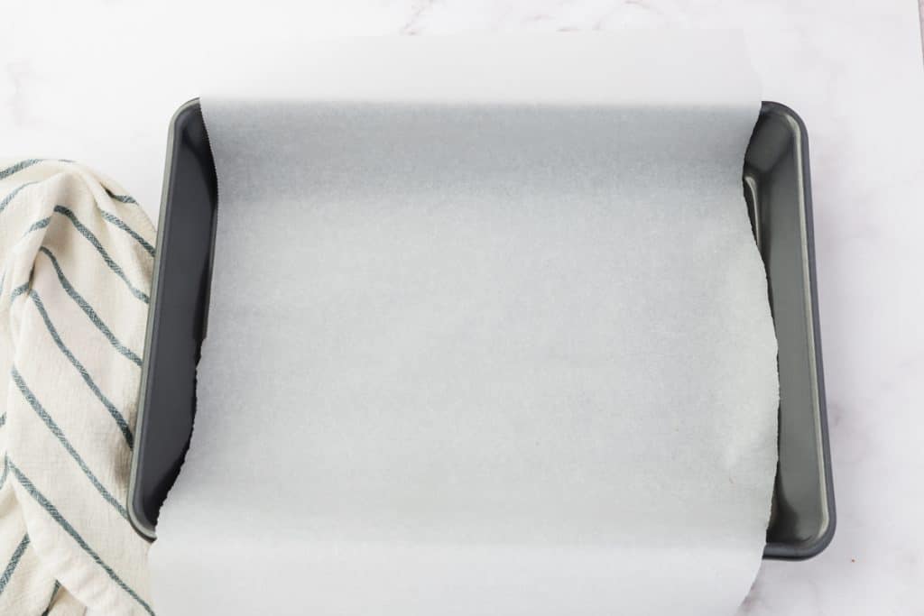 a 9 by 13 inch metal baking pan lined with parchment paper with extra hanging over the long sides.